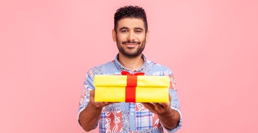 Ein junger Mann im bunten Hemd hält ein gelbes Paket mit roter Schleife hoch