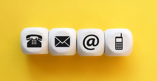 Vier Würfel auf gelbem Untergrund. Auf den Würfeln sind abgebildet: ein Telefon, ein Brief, ein @-Zeichen als Symbol für Mails und ein Mobiltelefon